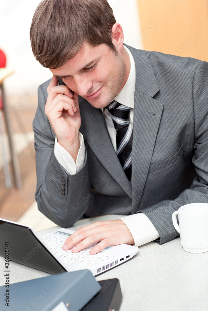 Fotografie Assertive businessman talking on phone and using his laptop