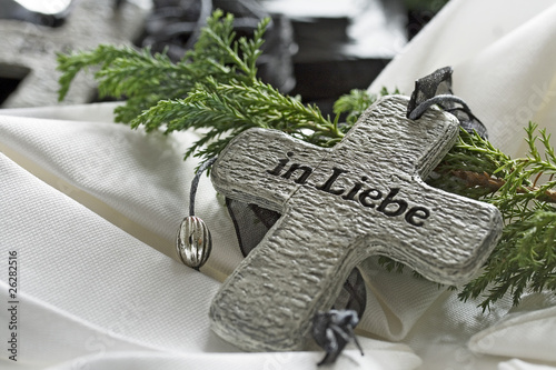 Trauerkreuz aus Stein mit der Aufschrift In Liebe auf weißem Tuch mit Tannenzweig als Grabschmuck für Beerdigung oder Totensonntag