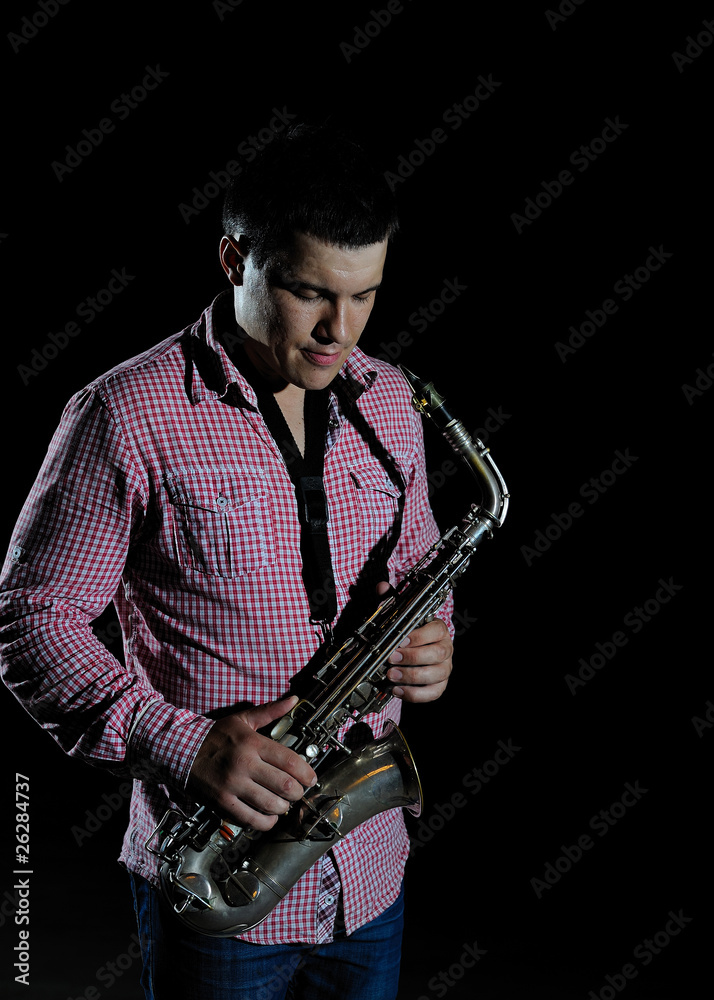 Naklejka premium Young handsome man playing music on saxophone. black background