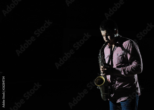 Young handsome man playing music on saxophone. black background