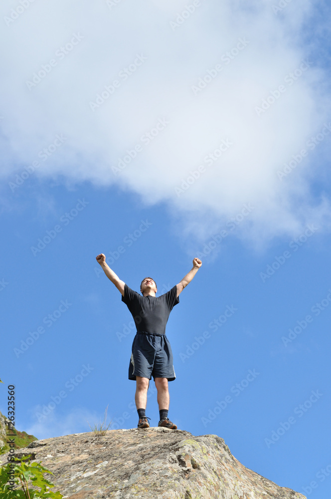 A young man stands on a cliff top and raised his hands A young man stands on a cliff top and raised his hands