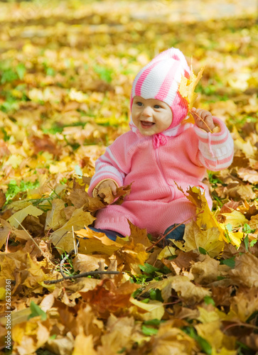 Baby girl playing with autumnal leaves
