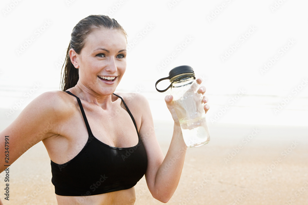 Healthy fit young woman on beach drinking water