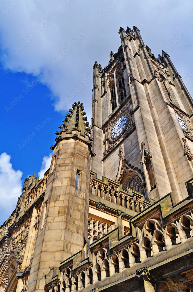 A detail of the facade of Manchester Cathedral backed by blue sky and white clouds in Manchester U.K.