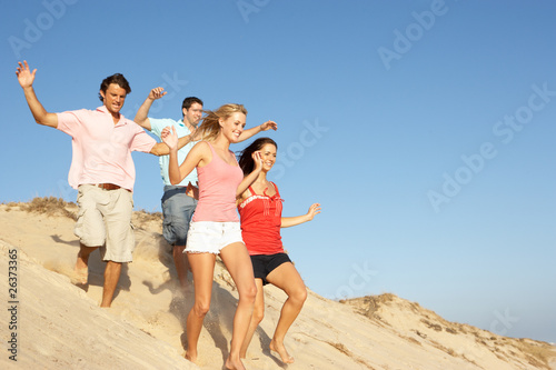 Group Of Friends Enjoying Beach Holiday Running Down Dunes