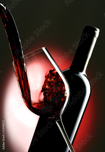 Pouring red vine into glass with bottle in the background.