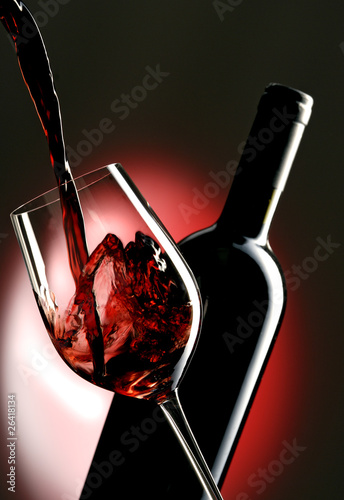 Pouring red vine into glass with bottle in the background.