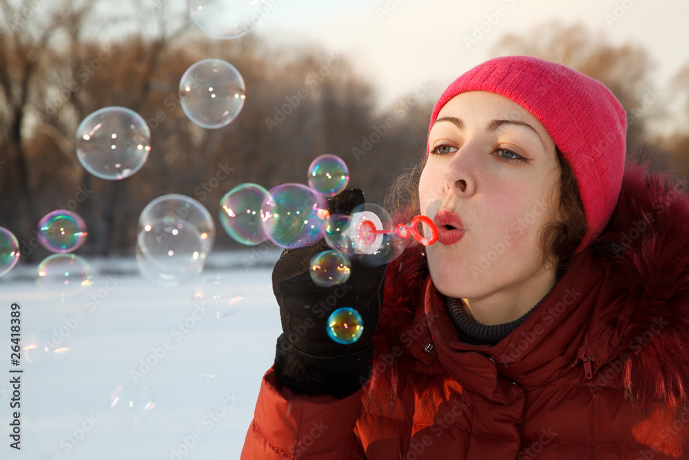 Girl blow bubbles in winter park. She is wearing jacket and hat.