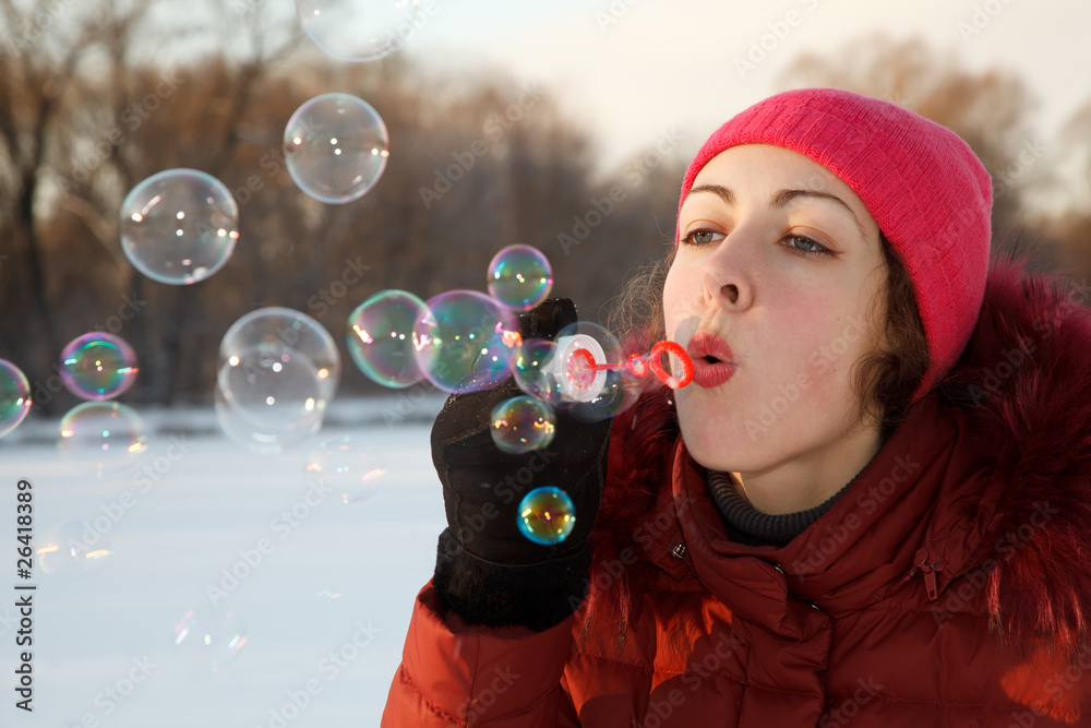 Girl blow bubbles in winter park. She is wearing jacket and hat. Girl blow bubbles in winter park. She is wearing jacket and hat.