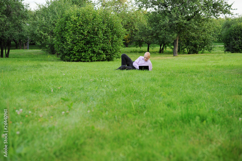 Businessman with laptop lying on green grass © Valeriy Lebedev