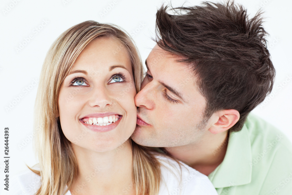 Careful man kissing his smiling girlfriend against a white backg Careful man kissing his smiling girlfriend against a white backg