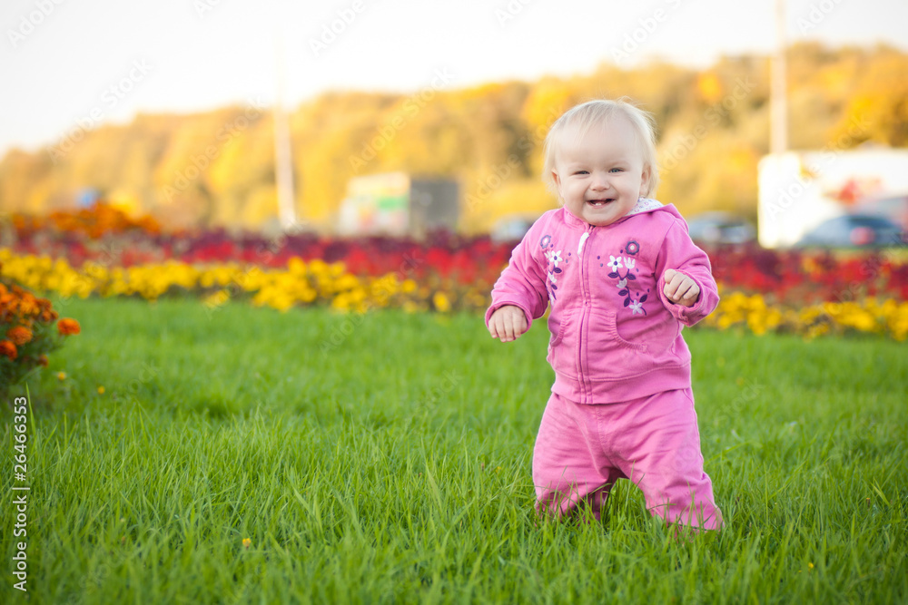 Cute cheerful baby walking on green grass among variety of flowe Cute cheerful baby walking on green grass among variety of flowe