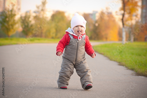 Young cheerful baby walking by asphalt road in park near street