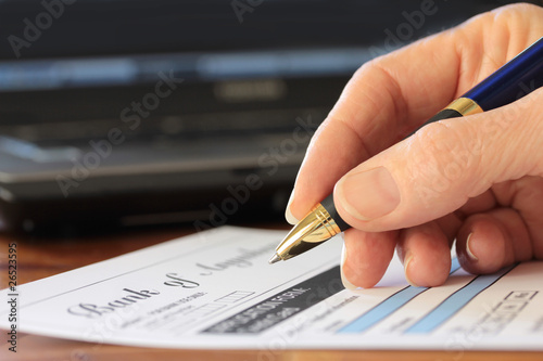 Hand with Pen Completing Fictitious Form Laptop in Background