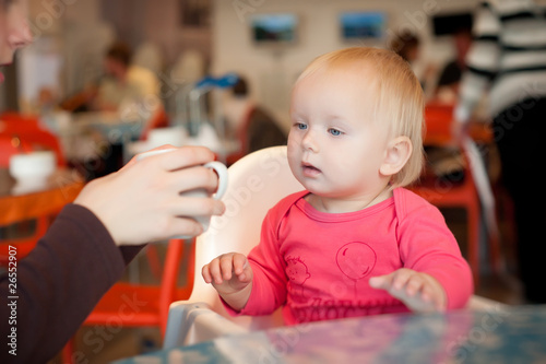 Adorable toddler girl sitting on chair in cafe with mother