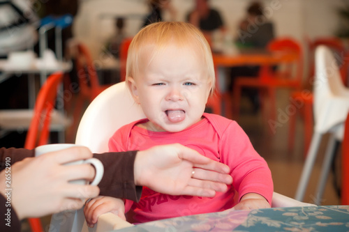 Adorable toddler girl sitting on chair in cafe with mother