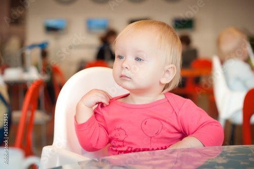 Adorable toddler girl sitting on chair in cafe near mother