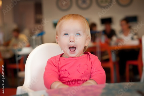 Adorable toddler girl sitting on chair in cafe near mother