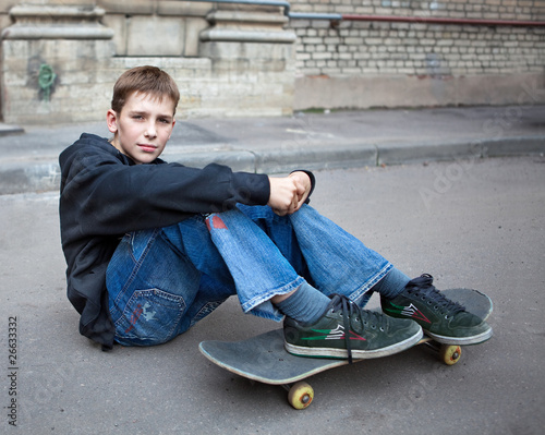 The teenager sits on asphalt with a skateboard
