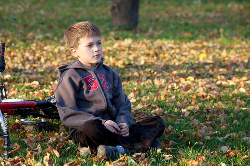 Мальчик сидит на траве  рядом с велосипедом