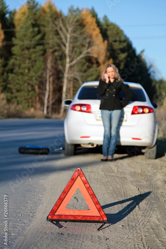 Young woman standing by her damaged car and calling for help