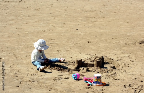 Child in a white hat builds sand castle