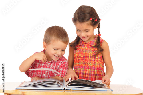 Two smiling children reading the book on the desk