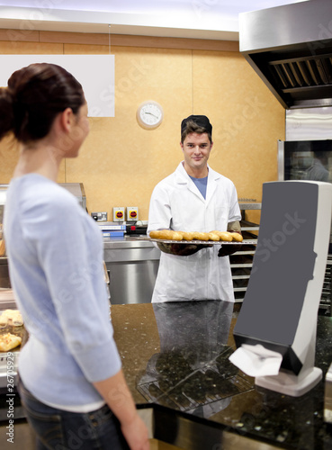 Young baker holding bread and baguette smiling at a customer in