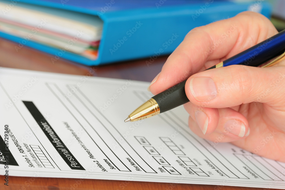 Hand with Pen Completing Personal Information on Form Hand with Pen Completing Personal Information on Form