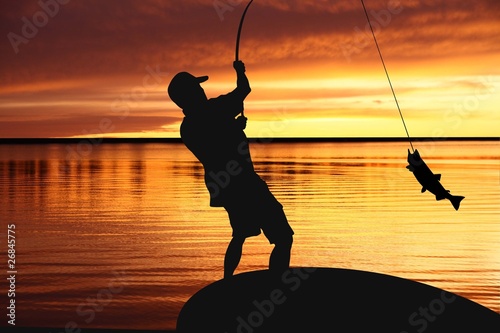 Leinwand Poster fisherman with a catching fish on sunrise background