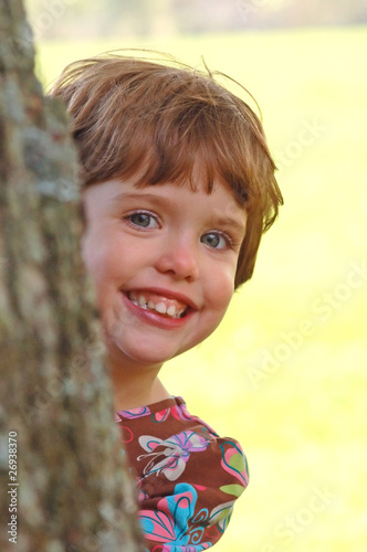 Child peeking from behind a tree