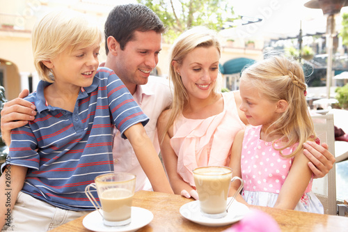 Young Family Enjoying Cup Of Coffee In Cafe Together
