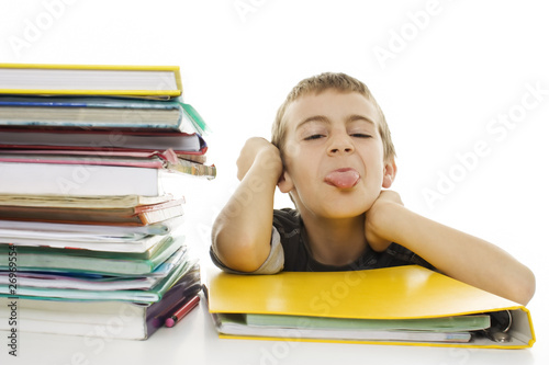 Child sticks out his tongue with school books on the table
