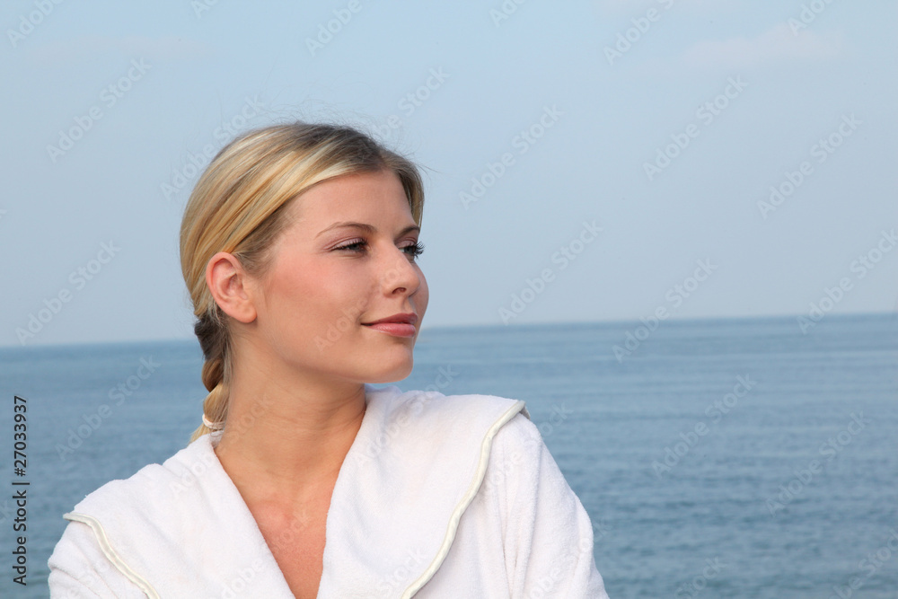 Smiling beautiful woman standing by the sea in bathrobe Smiling beautiful woman standing by the sea in bathrobe