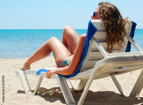 sexy woman is lying on chaise longue near a sea, view from behin photo