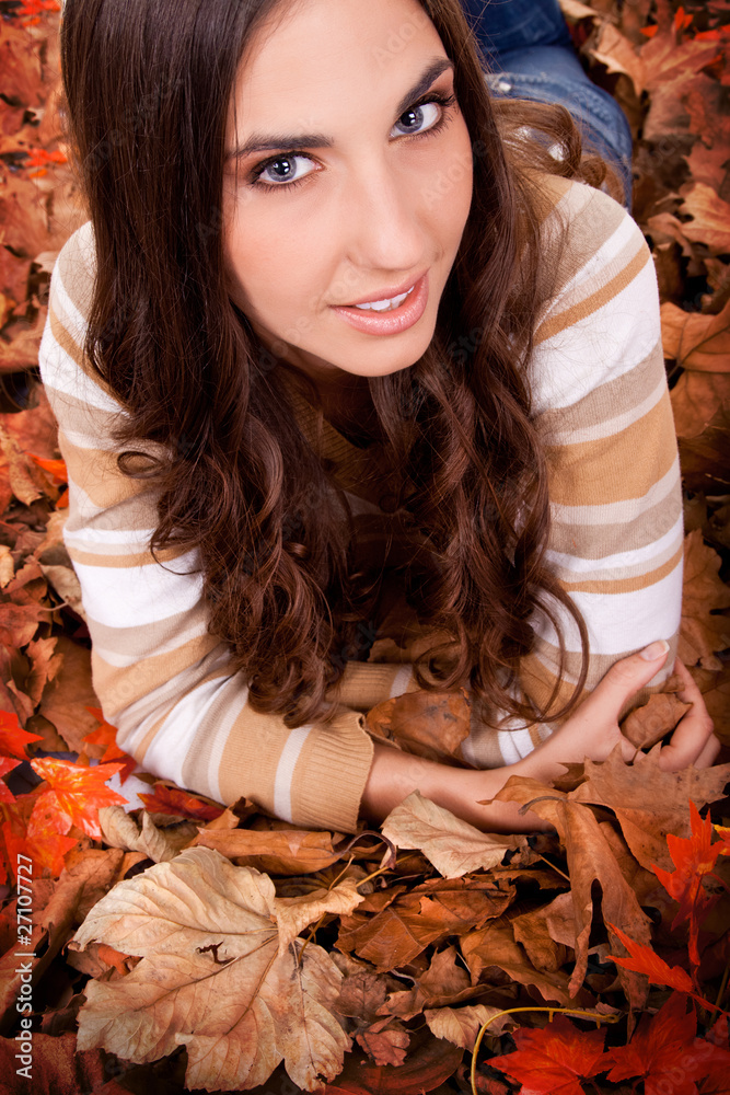 brunette woman lying on autumn leaves