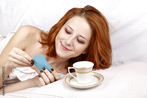 Woman in white lying in the bed near cup of coffee.