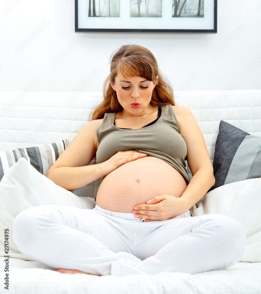pregnant woman sitting on sofa and blowing kiss her belly. pregnant woman sitting on sofa and blowing kiss her belly.