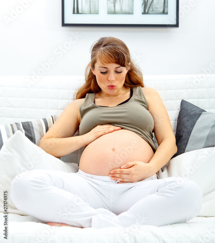 pregnant woman sitting on sofa and blowing kiss her belly.