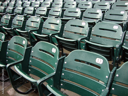 Rows of empty wet green stadium seats, seats number 13, 12, 11