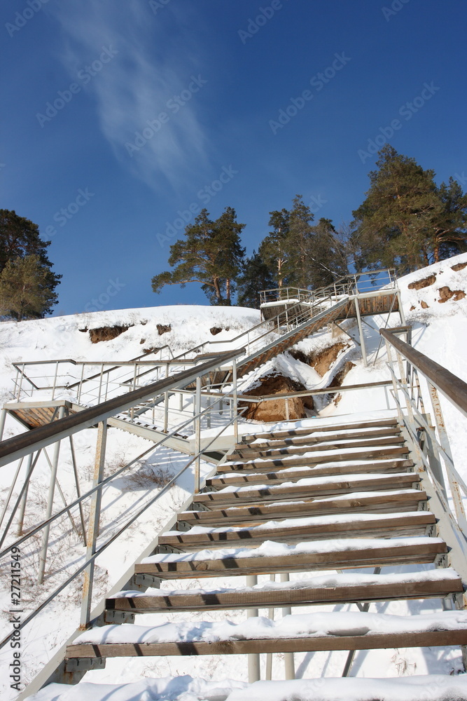 Stairs with landing against a snow slope against pines