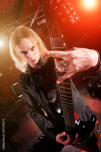 Long haired guitarist is playing and and making a rock hand gest
