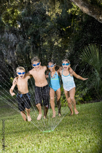 Children running through lawn sprinkler together