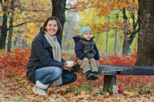 Little cute boy drinks tea with her mother in autumn park