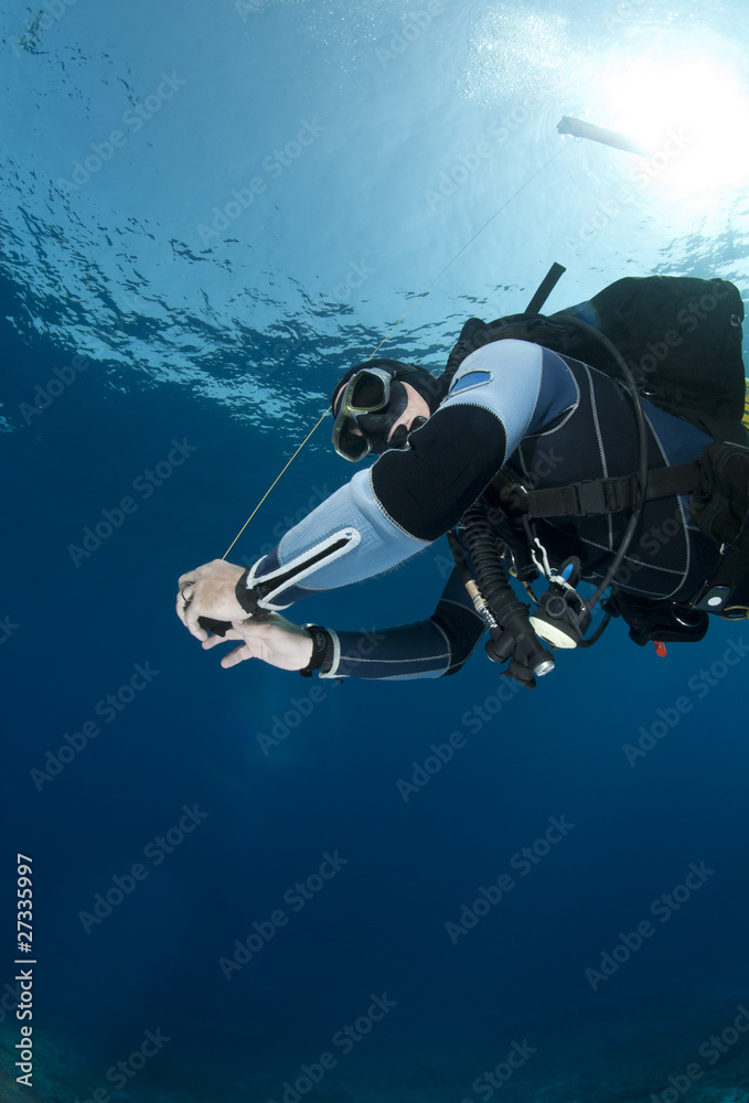 Adult male scuba diver holding a surface marker buoy underwater
