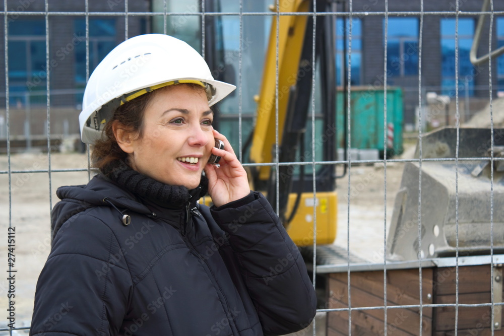 Bauleiterin telefoniert lächelnd auf einer Baustelle