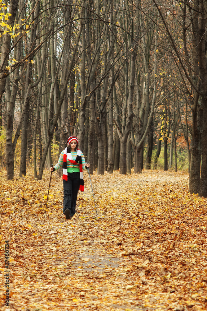 woman with Nordic walking sticks in autumn forest alley
