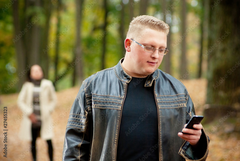 Fototapeta premium Man in park with girlfriend in background. Man call on phone