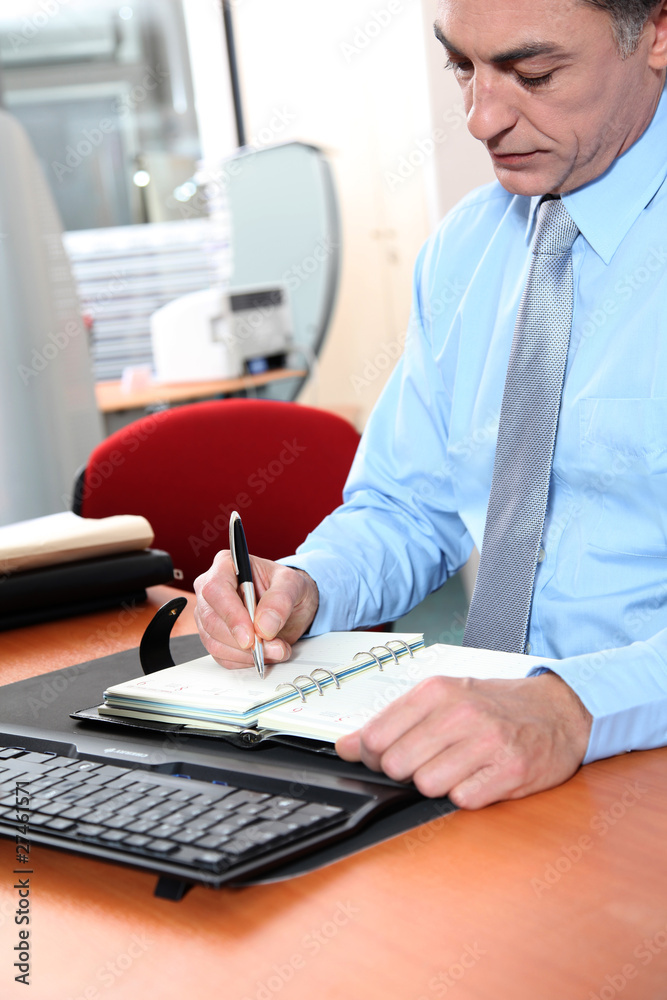 Businessman at his desk writing down on his agenda Businessman at his desk writing down on his agenda
