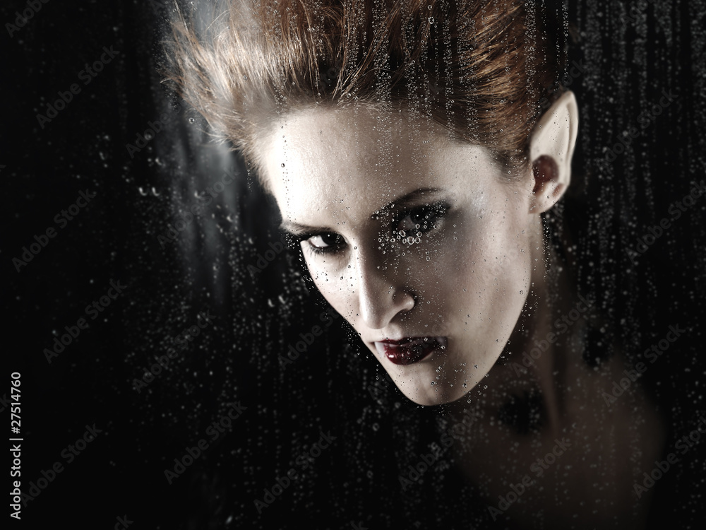 Portrait of a beautiful fashion vampire woman behind rainy windo
